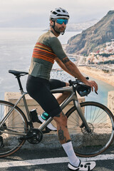 A cyclist in stylish gear pauses on a scenic coastal road,overlooking a charming town.His bike and...
