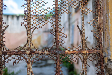 A close-up of a rusty metal fence with intricate details, set against a blurred and colorful background, symbolizing decay and vibrant contrasts