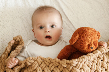 Cute little baby lying in crib with teddy toy under cozy knitted blanket. Bedtime. Adorable infant...
