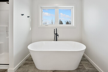 A white bathtub with a black faucet sits in a bathroom with a window