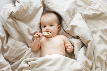 Cute little baby lying in beige sheets with ooden teether. Time to bed or wake up. Happy adorable...