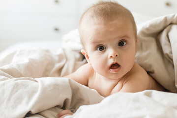 Adorable baby lying in beige sheets in morning light. Time to sleep or wake up. Happy cute infant portrait on bed, space for text. Child sleep and childcare