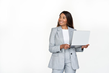 Happy African American business woman using laptop standing isolated on white background. Smiling professional businesswoman executive wearing suit holding computer working online looking away.
