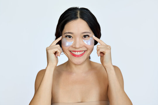 Happy smiling mature Asian woman model advertising antiage face skin care undereye hydrogel patches cosmetic treatment to reduce puffiness under eyes looking at camera isolated on white background.