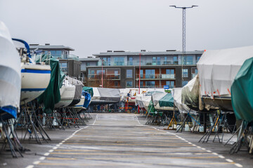 covered boats on metal stands in marina or boatyard on overcast day.
