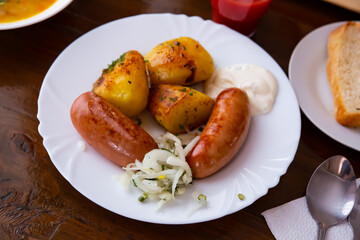 Fried big sausages, potatoes divided in half dished up in a plate with fresh chopped onion and mayonnaise