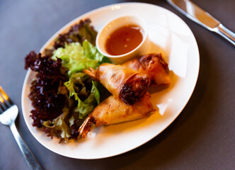 Fried spring rolls with vegetables and shrimps, served on ceramic plate with sauce and salad..