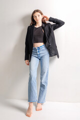 Stylish young woman poses confidently in casual attire with black blazer and jeans in a minimalist...