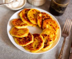 National dish syrniki served on white circular plate with smetana and serving pieces.