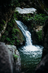 Fototapeta premium Close-up of a picturesque waterfall cascading over moss-covered rocks into a calm, clear pool surrounded by vibrant greenery in a serene natural setting