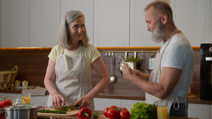 Caucasian couple middle-aged family woman man cook breakfast in home kitchen senior wife chop fresh vegetables healthy food mature husband take photo record video blog on mobile phone cooking dinner