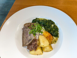 Tyrolean Tafelspitz main course dish, tender boiled Beef, fried potatoes, cream spinach and garnish in white plate on table