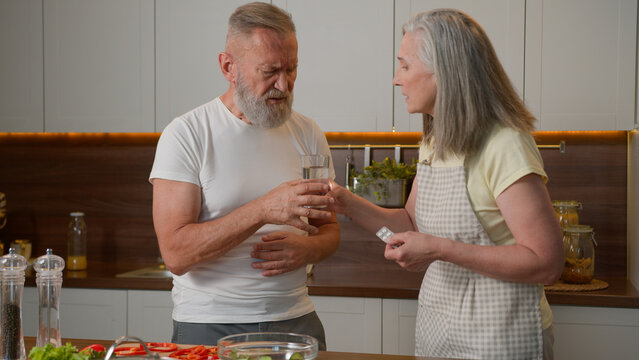 Sick unhealthy old man in kitchen feeling pain in chest heart attack heartache bad health cardiac medical problem Caucasian family caring mature woman wife help husband give remedy tablet drink pill