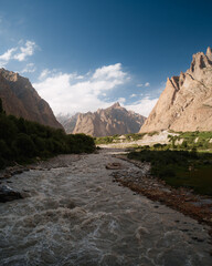 River flows through hushe valley, surrounded by towering mountains under a clear sky