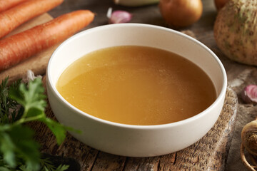 Chicken soup or bone broth in a white plate with fresh vegetables