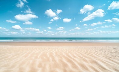 Tranquil beach with rippling sand under a clear blue sky with floating clouds