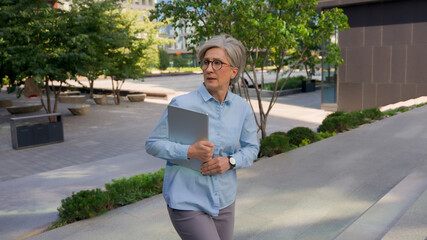 Old Caucasian businesswoman mature woman professional business lady walking up stairs in city...
