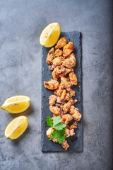 chipirones sobre un fondo de concreto en un plato negro con imagenes cenitales y acompañado de limones todo con colores neutros.