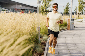 Energetic jogger enjoys morning run in urban park with tall grass and modern architecture