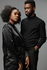 Stylish couple posing together with confident expressions, showcasing modern fashion in a minimalist gray background, representing love and connection