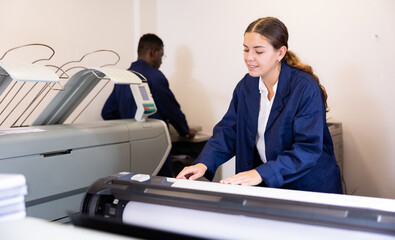 Woman working in publishing facility, loading large format paper in printer