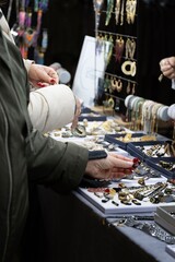 A stylish shot of an adult woman browsing through an array of jewelry pieces at a market. 