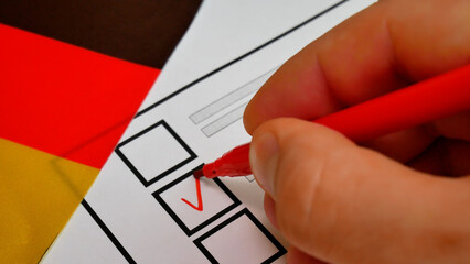 Electoral decision in Germany. Voters hand votes using red felt-tip pen, marking candidate with check. German national colors in background. Representation of democracy, voting rights