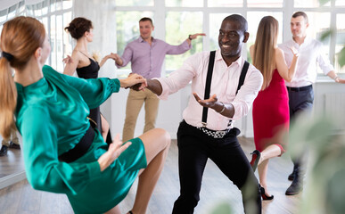 Woman in elegant evening dress dances incendiary boogie woogie with African American man partner...