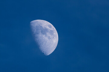 A large half moon is in the sky above a blue sky