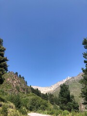 Obraz premium A bright sunny day in the mountains, with lush green trees covering the slopes. The clear blue sky and warm sunlight create a breathtaking and peaceful natural landscape. 