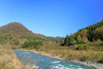 静かに流れる姫川の側から紅葉の長野県小谷村の風景と大糸線を望む