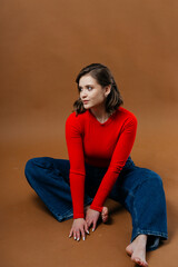 A fashionable young woman in a bold red top and wide-leg denim jeans strikes a dynamic and artistic...
