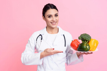 Portrait of smiling female doctor in white gown with stethoscope holding plate of vegetables...