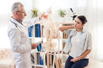 Doctor in white gown with stethoscope and female patient in office. Patient's neck hurts.