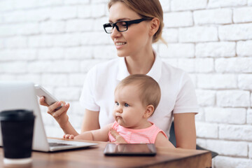 Mother with baby working and using smartphone. Motherhood concept.