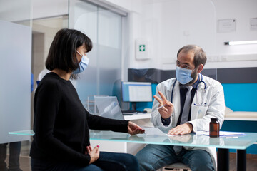 Young woman sitting at desk and receiving prescription paper from doctor during clinic appointment. Male physician giving medical document and explains treatment plan to female patient in hospital.