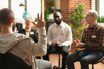 Selective focus on young guy making gestures with his hand during therapy session. Group of diverse...