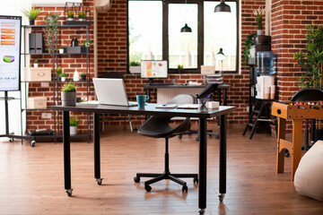 Startup office with modern furniture and company data displayed on screens of digital devices. Indoor decorations include foosball table, plants and water cooler, representing contemporary workspace.