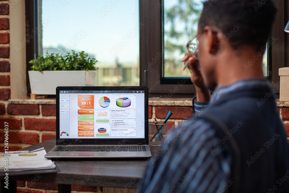 Poster rearview of african american analyst deeply focused on reviewing business summary analytics displaye