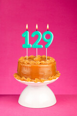 Birthday cake with number 129 candle - Anniversary card on a pink background.