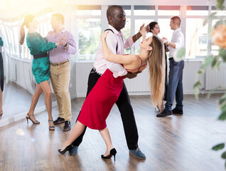 Woman in elegant evening dress dances incendiary tango with African American male partner during...