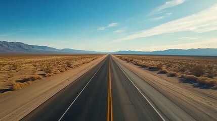 Fototapeta premium Endless Road stretches towards Mountains Under Clear Blue Sky Horizon
