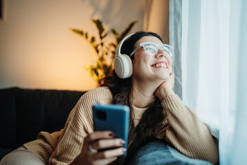 Young caucasian woman listening to music and singing by the window	