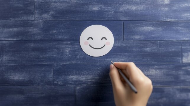 World Compliment Day concept. A hand drawing a smiling face on a white circle against a blue wooden background.