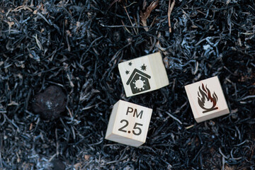 Three wooden blocks scattered on burnt ground, featuring home pollution, PM 2.5, and fire icons,...