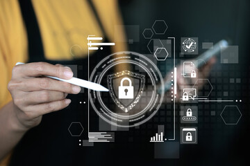 A person is holding a pen and pointing at a screen with a security symbol. The screen has a lot of icons and the person is looking at the screen