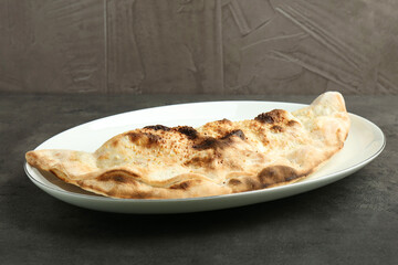 One delicious calzone on grey textured table, closeup