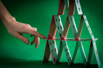 Woman destroying house of playing cards on green background, closeup