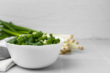 Chopped green onion in bowl and stems on white table, closeup. Space for text