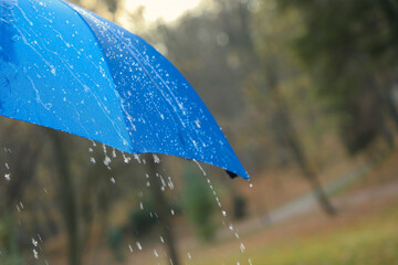 Open blue umbrella under pouring rain outdoors, closeup. Space for text